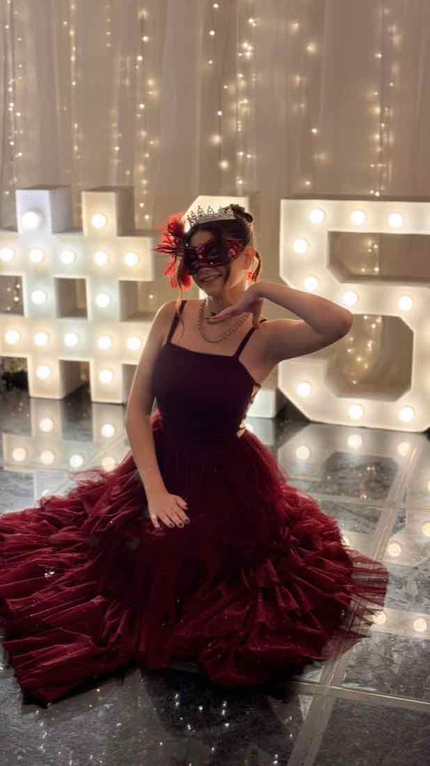 Debutante de vestido marsala diante das letras luminosas de 15 anos