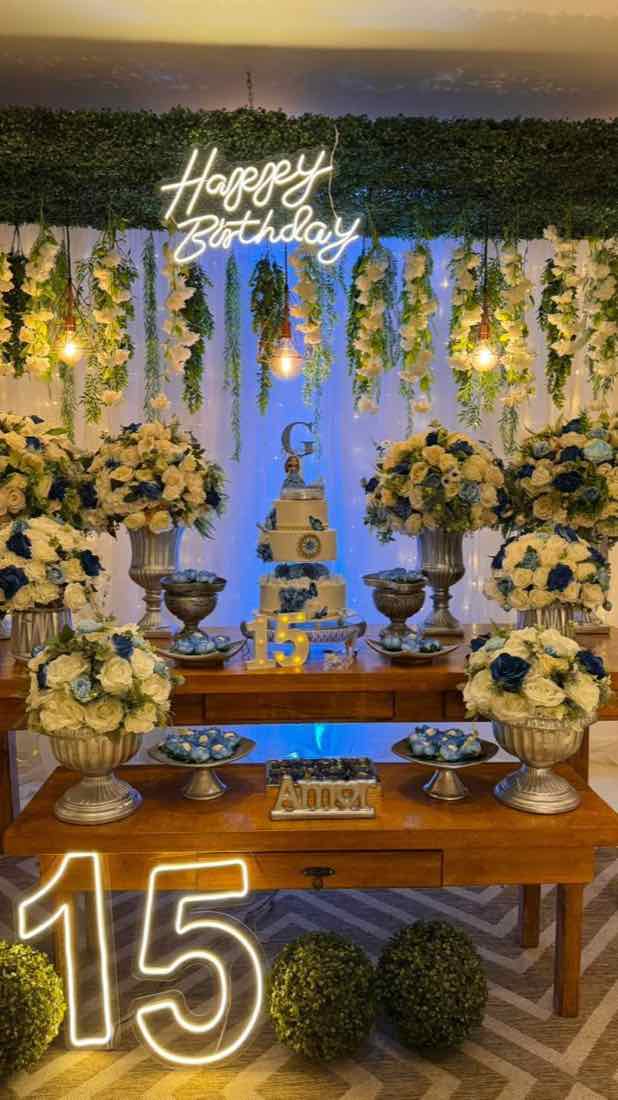 Mesa de aniversário com neon Happy Birthday e arranjos de flores